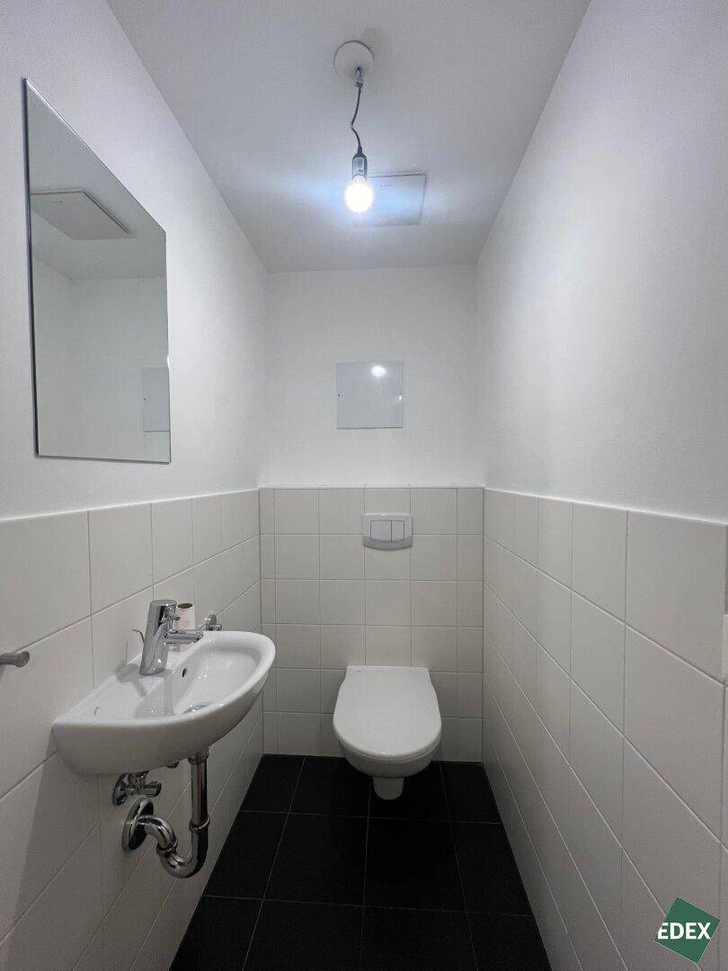 Kleines Gäste-WC mit Waschbecken, wandhängender Toilette und dunklem Fliesenboden.