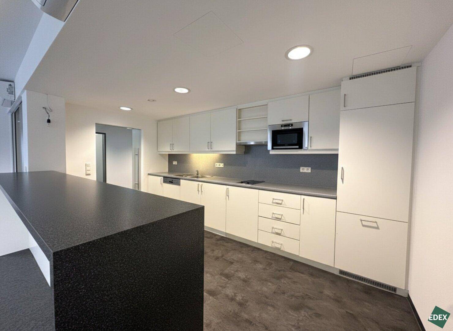 Moderne Einbauküche mit weißen Schränken, dunkler Arbeitsplatte und integrierten Geräten.