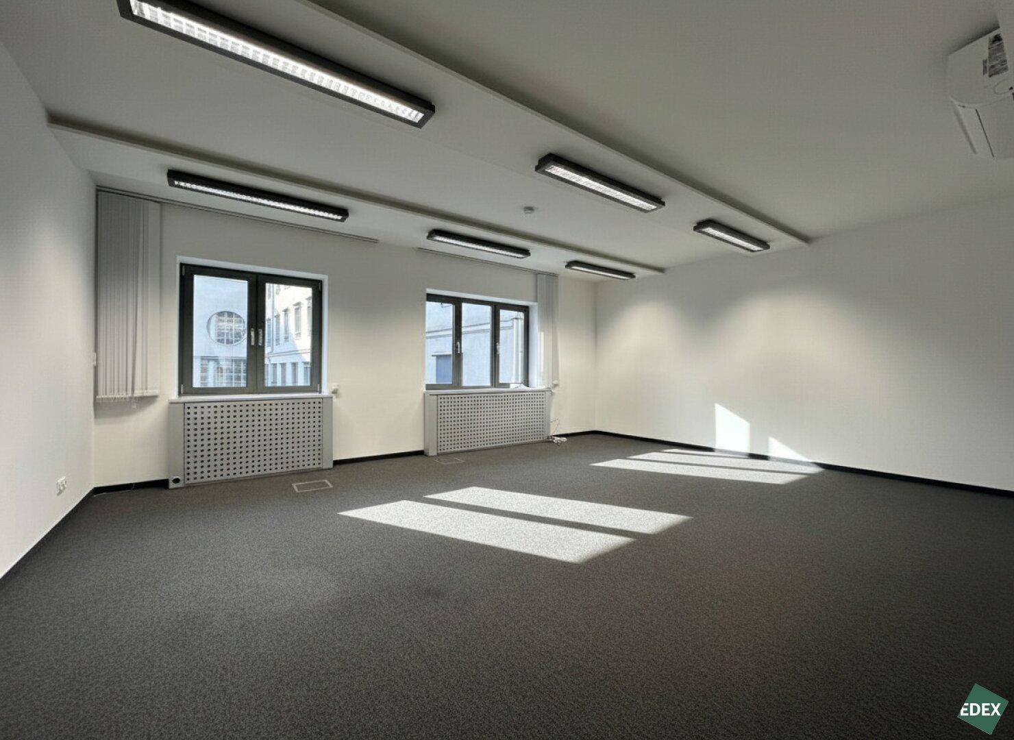 Geräumiges Büro mit Teppichboden, großen Fenstern und viel natürlichem Lichteinfall.