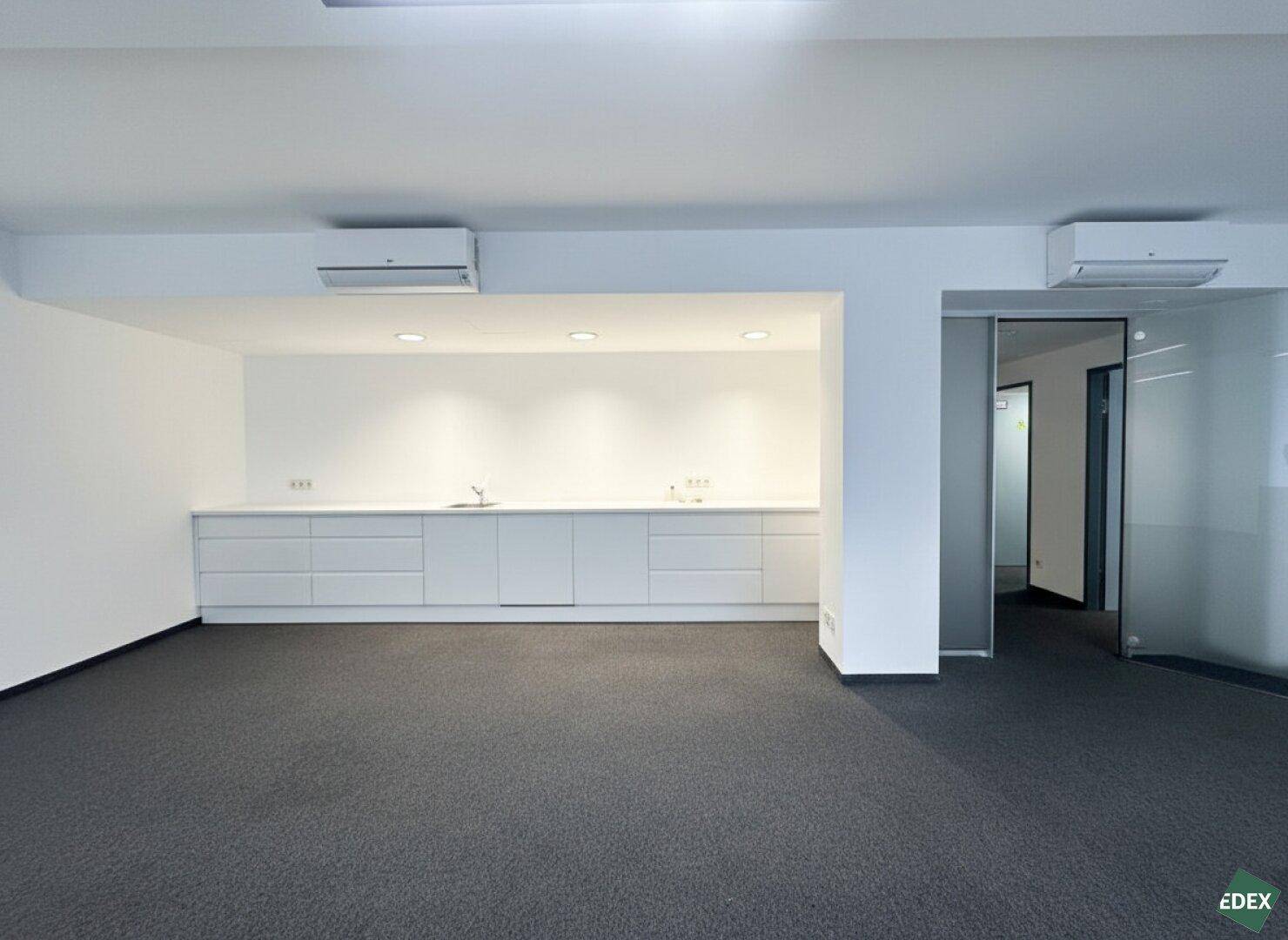 Modernes Büro mit Teppichboden, integrierter Küchenzeile und Klimaanlage.