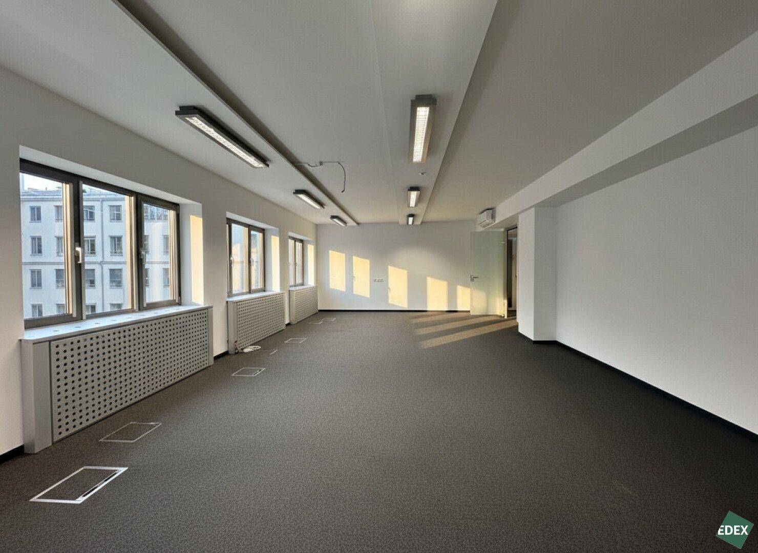 Helles Büro mit Teppichboden, großen Fenstern und Bodentanks für Strom und Daten.