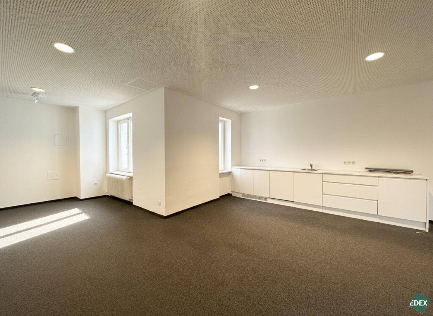 Heller Raum mit integrierter Küchenzeile, weißen Schränken und Teppichboden.