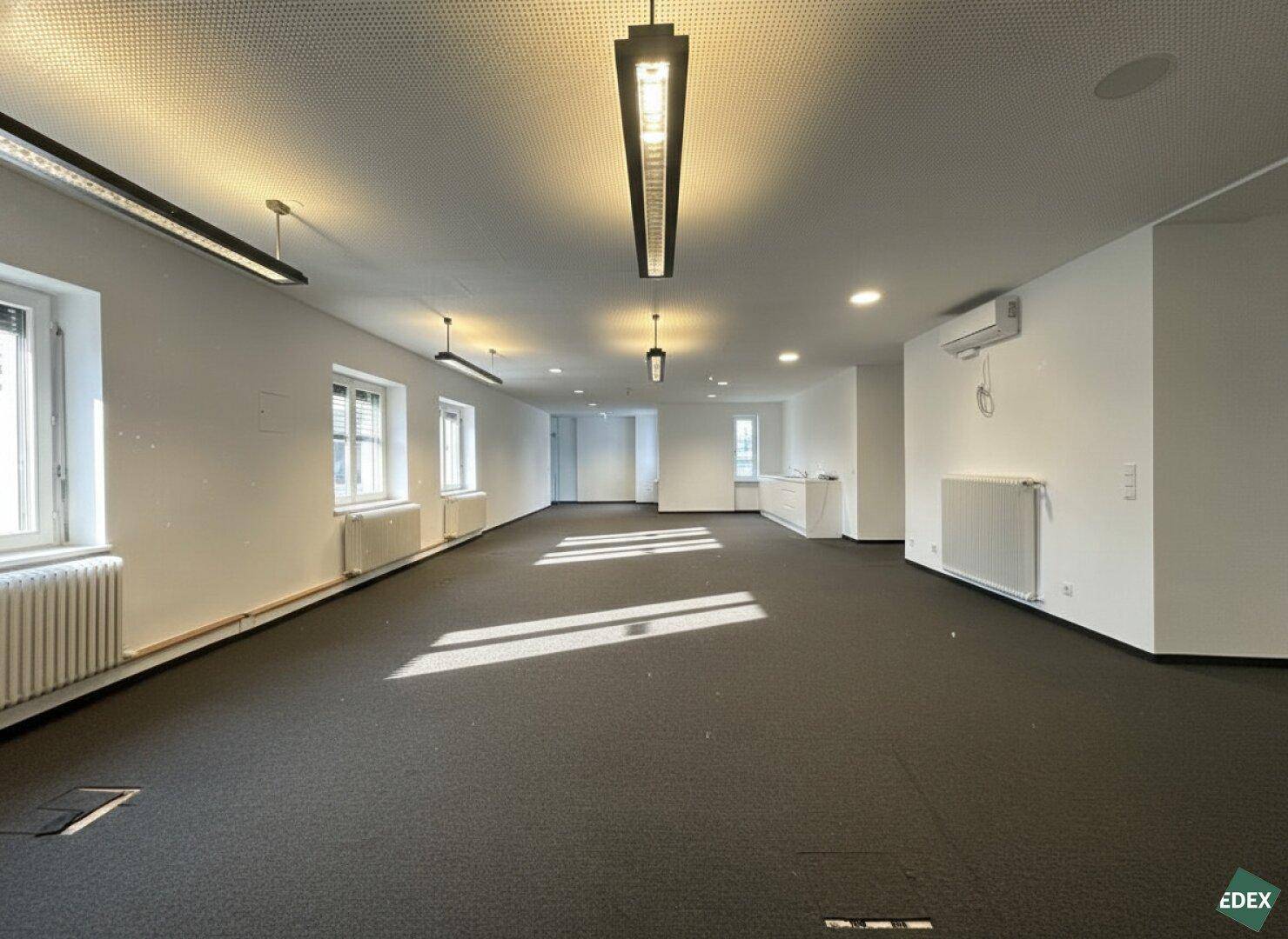 Heller Bürobereich mit Teppichboden, modernen Deckenleuchten und Klimaanlage.