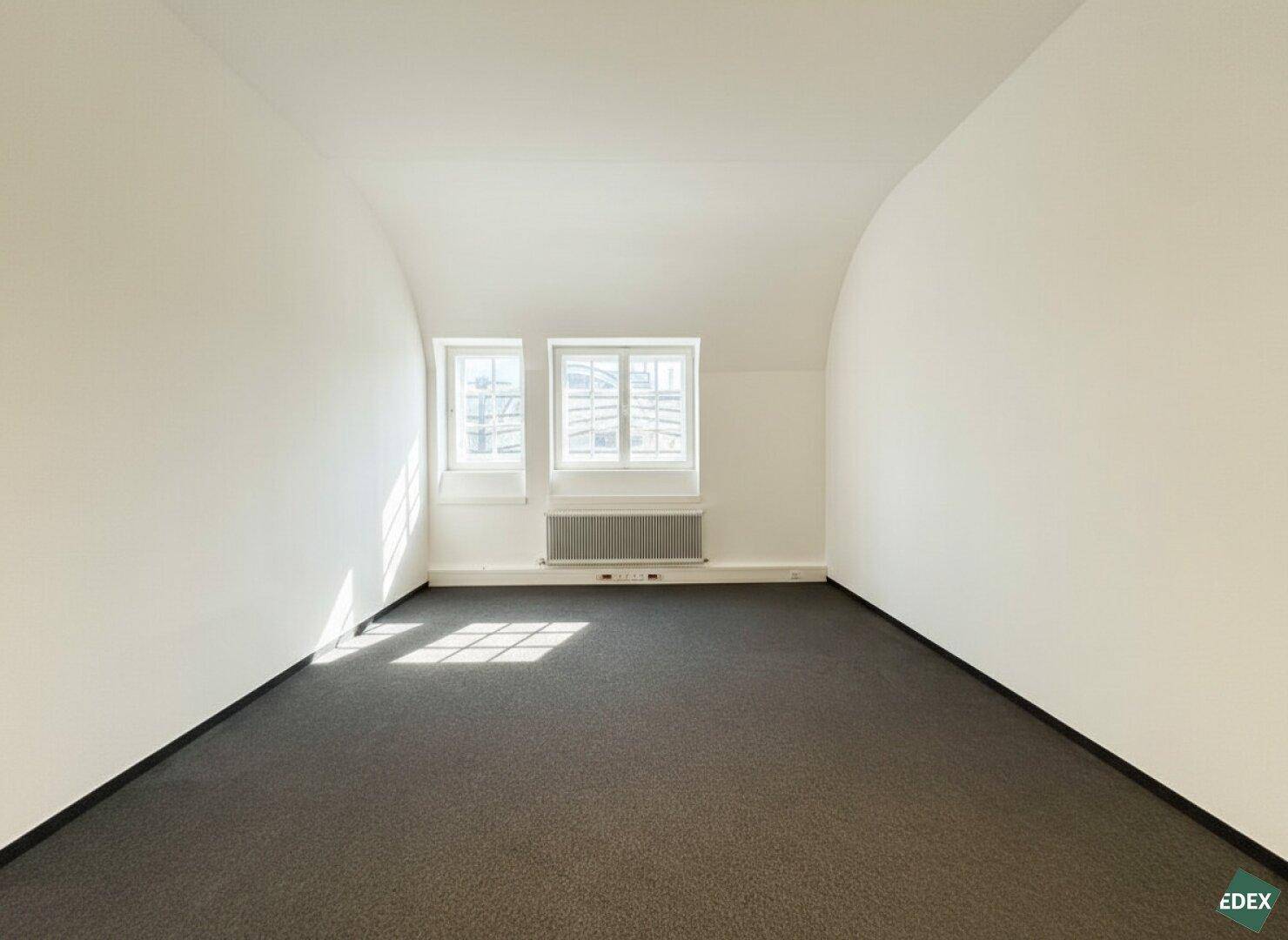 Kleinerer Büroraum im Dachgeschoss mit Teppichboden und zwei Fenstern.