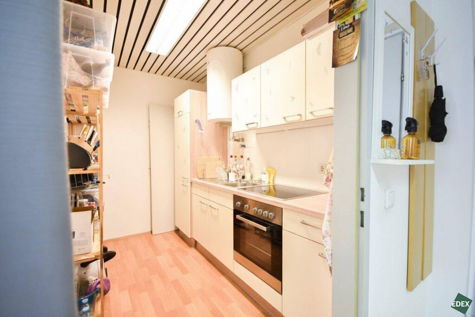 Schmale Küche mit hellen Einbauschränken, integriertem Backofen und einer Decke mit Holzlamellen.