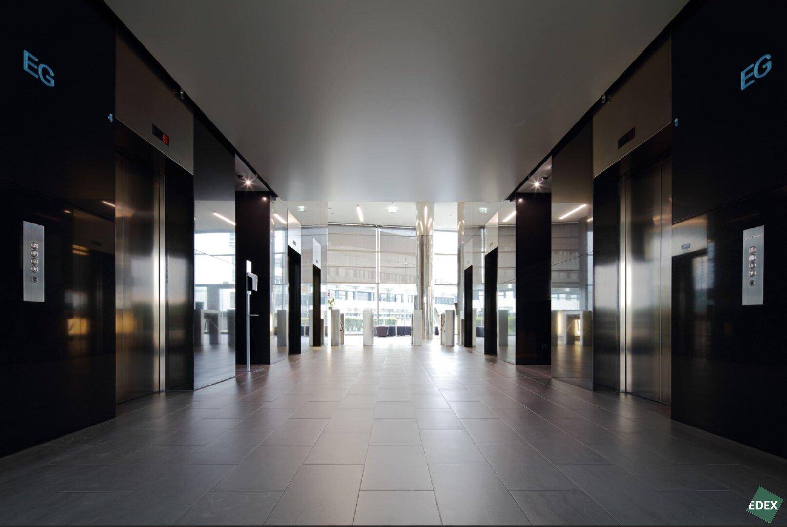 Elegante Lobby mit mehreren Aufzügen, dunklen Oberflächen und hellem Boden, die einen modernen Empfangsbereich bildet.