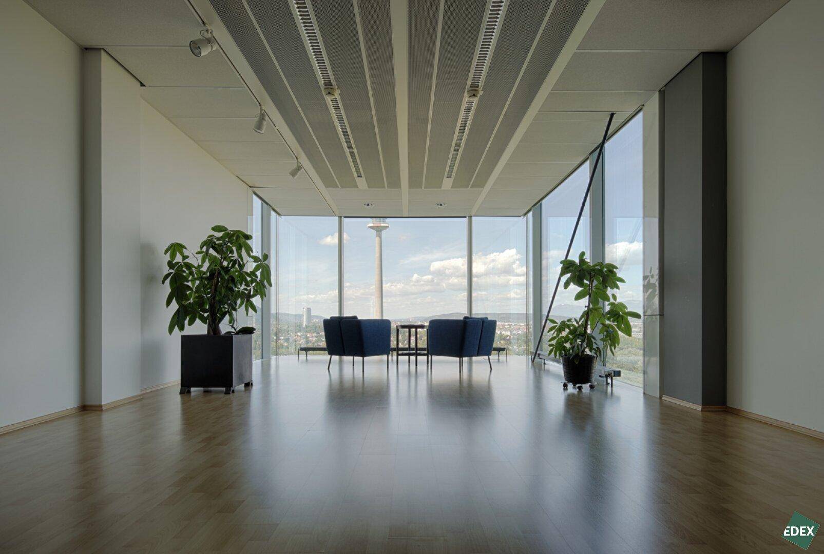 Geräumige Lobby mit Holzboden, großen Fenstern und bequemen blauen Sesseln mit Stadtblick.