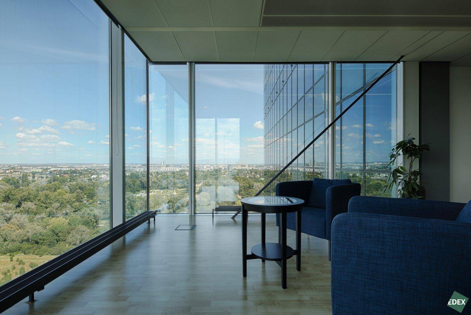 Gemütlicher Loungebereich mit großen Glasfenstern, die einen weiten Blick über die Stadt und Natur bieten.