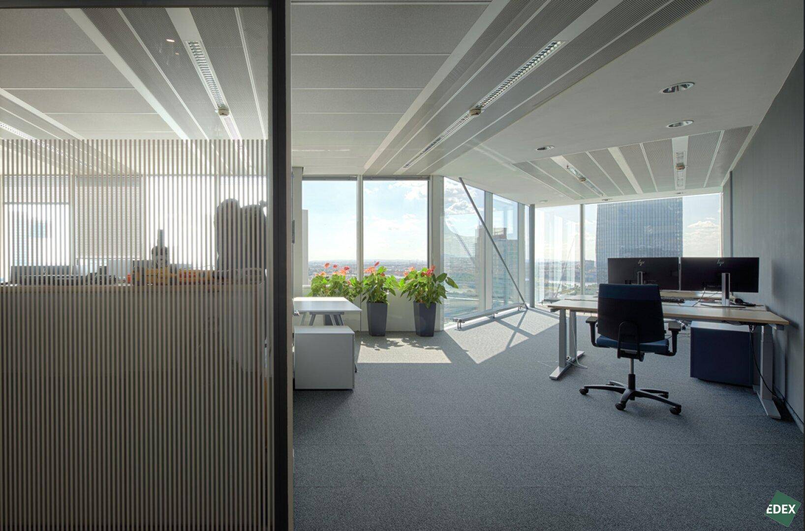 Modernes Büro mit Schreibtischen, Bürostühlen und großen Fenstern mit weitem Ausblick.