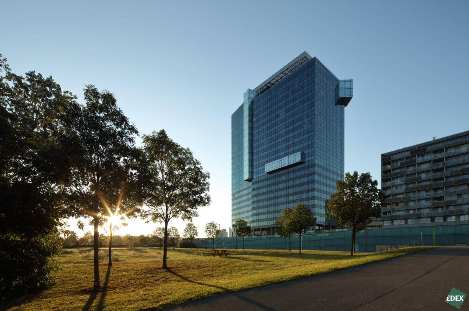 Modernes Bürogebäude bei Sonnenuntergang, umgeben von Grünflächen und Bäumen.