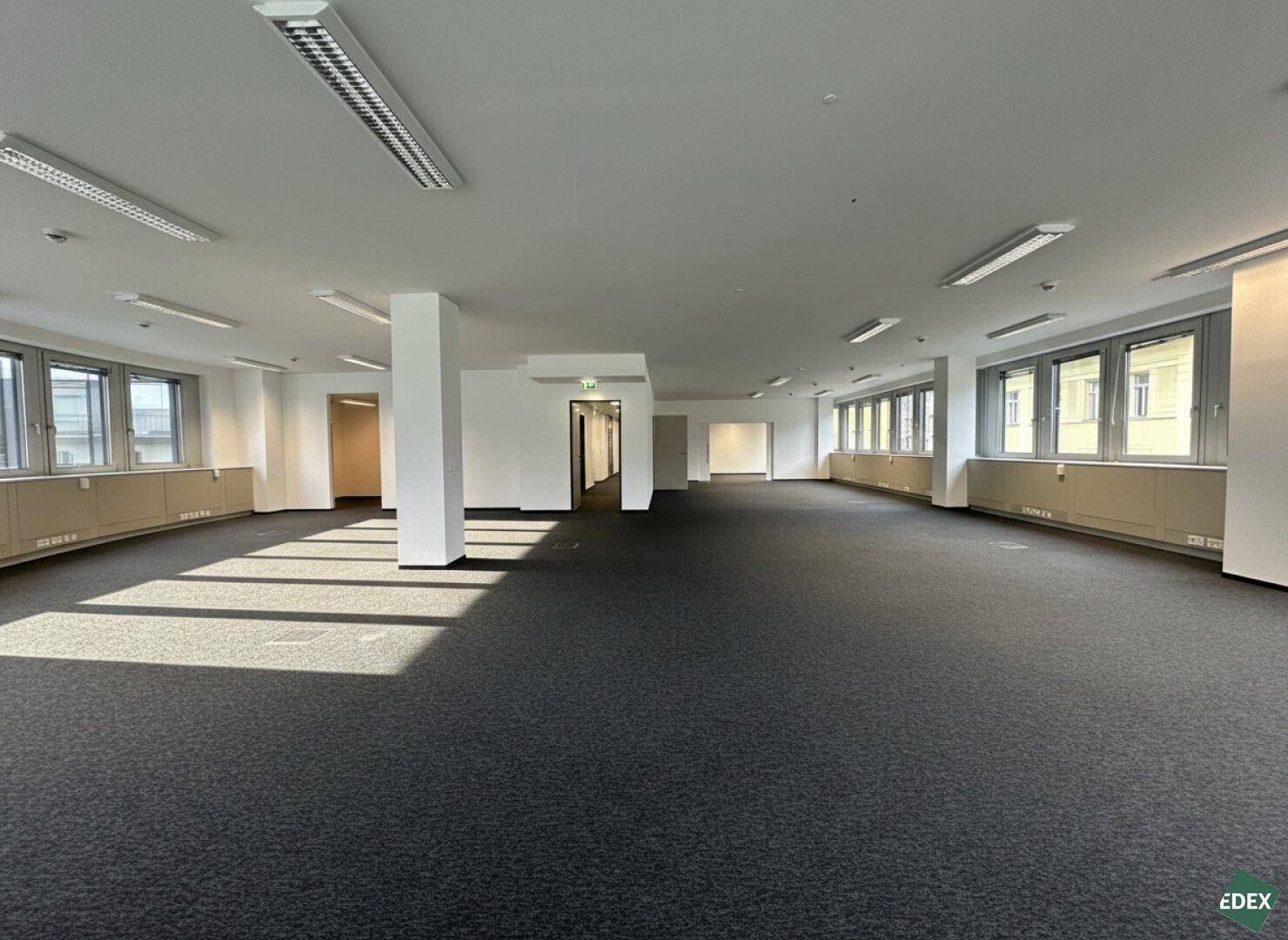 Weitläufiger Bürobereich mit Teppichboden, Säulen und natürlichem Lichteinfall durch zahlreiche Fenster.