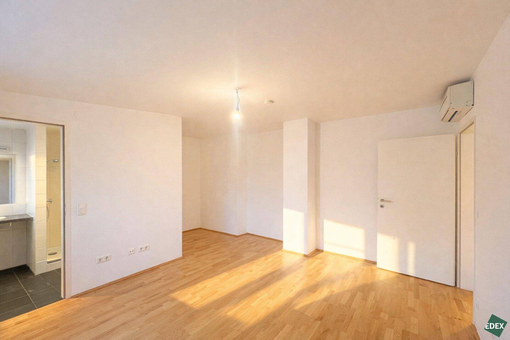 Heller Raum mit Holzfußboden und Zugang zu einem modernen Badezimmer mit Dusche.