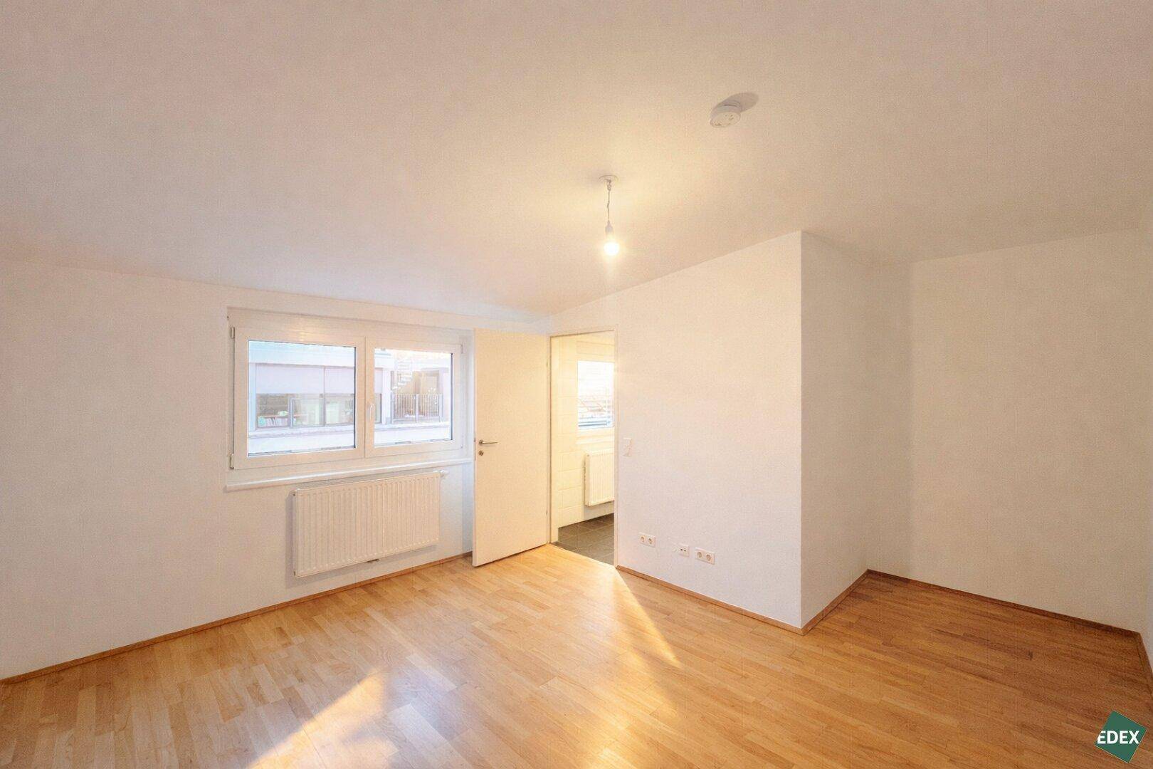 Schlafzimmer mit Holzfußboden, großem Fenster und Heizkörper, ideal für individuelle Gestaltung.