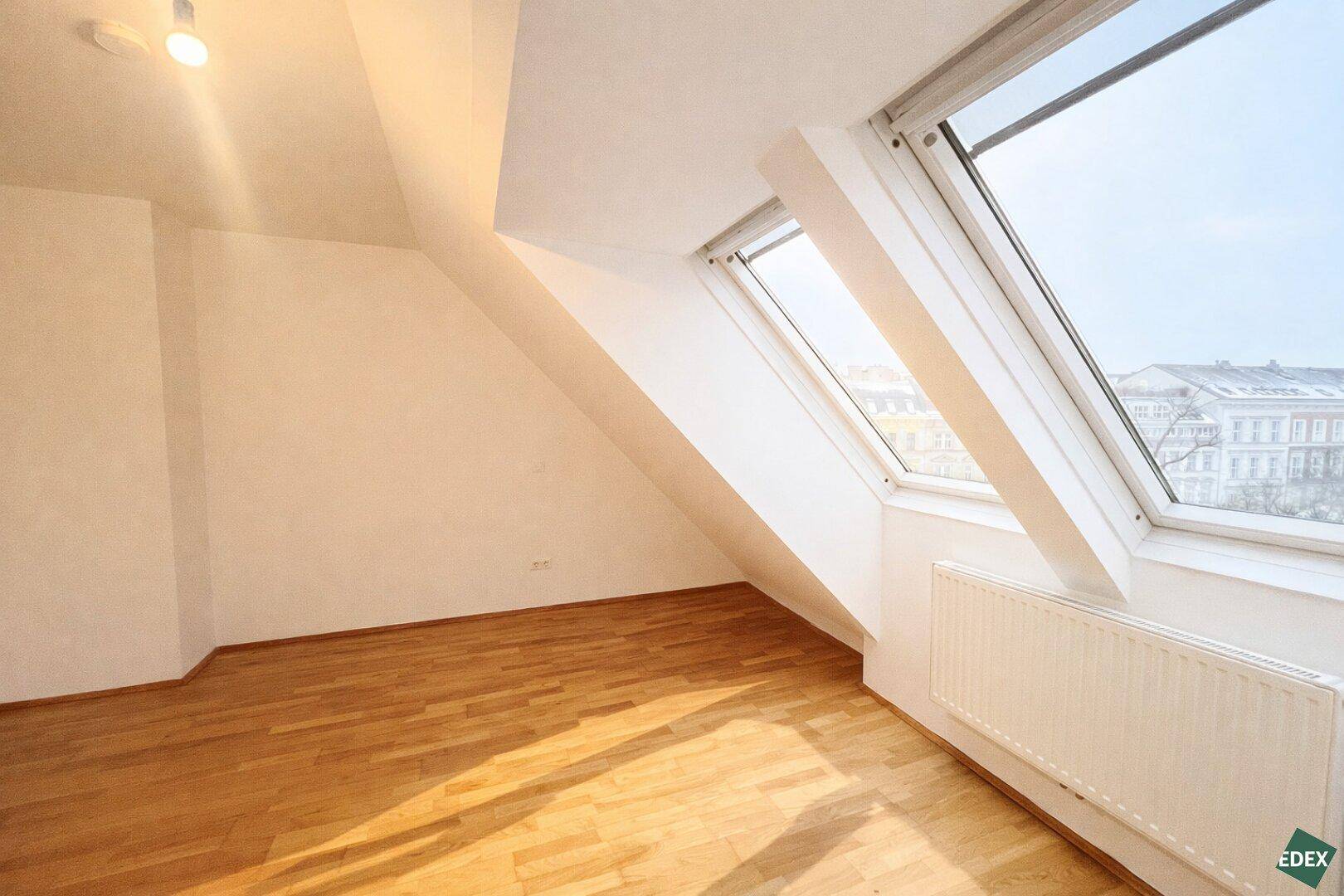 Helles Schlafzimmer mit Holzfußboden und schrägen Dachfenstern, die eine einzigartige Atmosphäre schaffen.