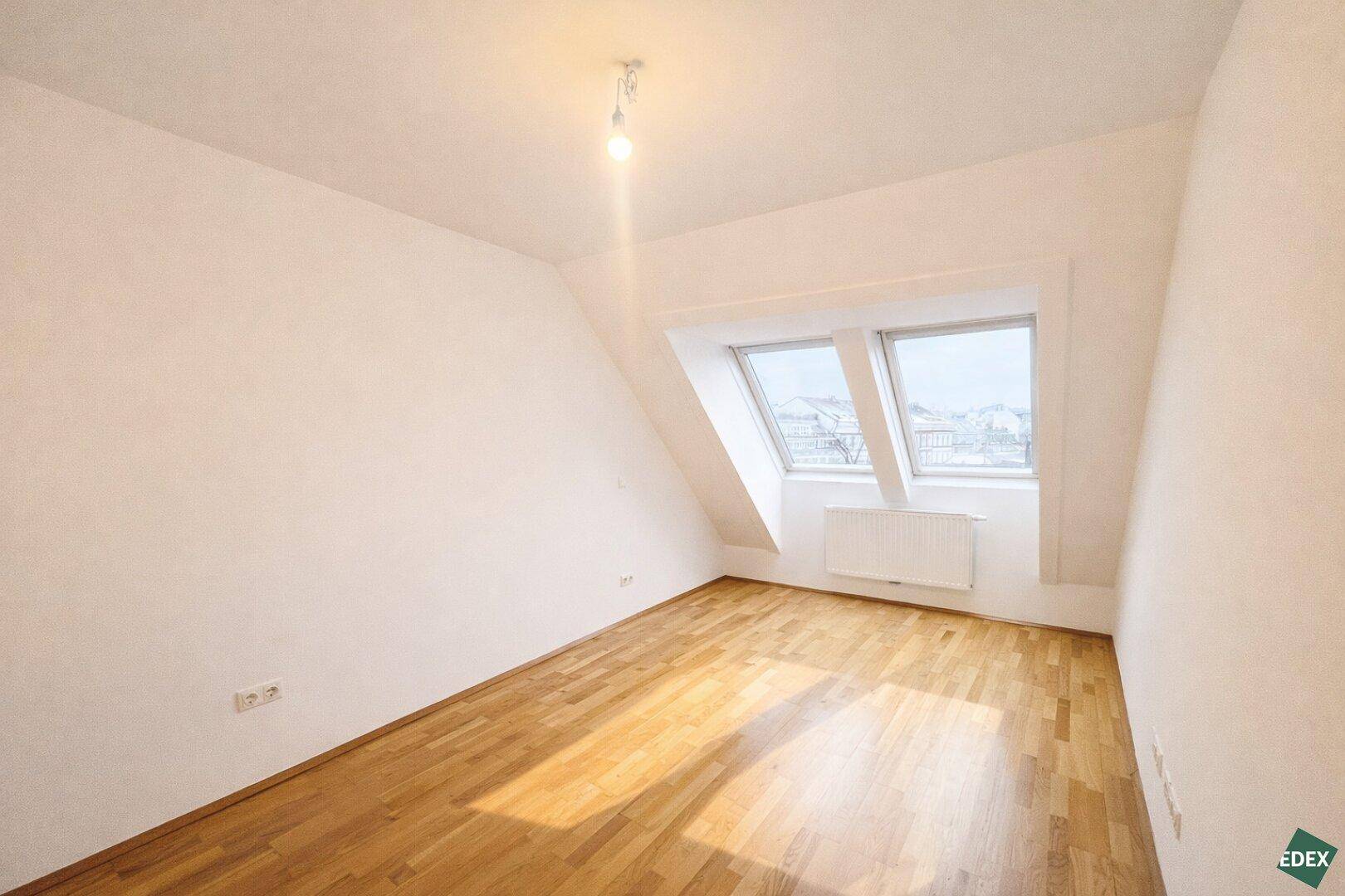 Geräumiges Schlafzimmer mit Holzfußboden und zwei Dachfenstern, die viel Licht hereinlassen.