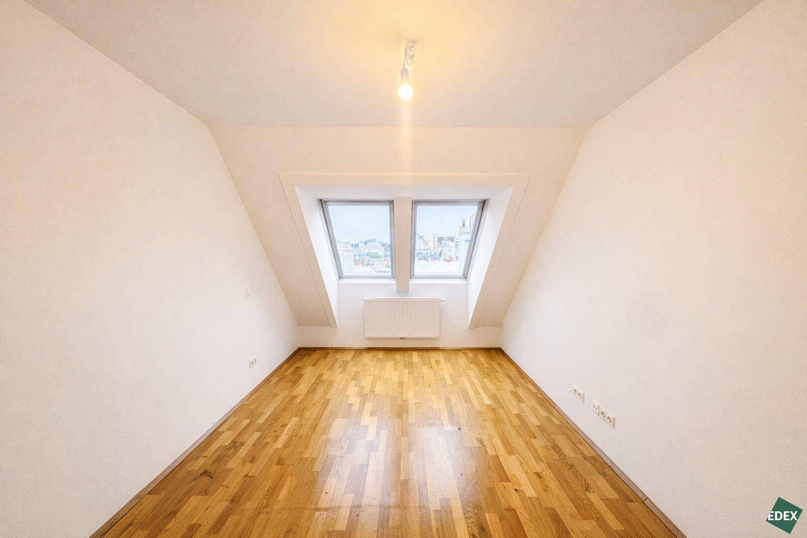 Schlafzimmer im Dachgeschoss mit Holzfußboden und einem großen Dachfenster, das den Raum erhellt.