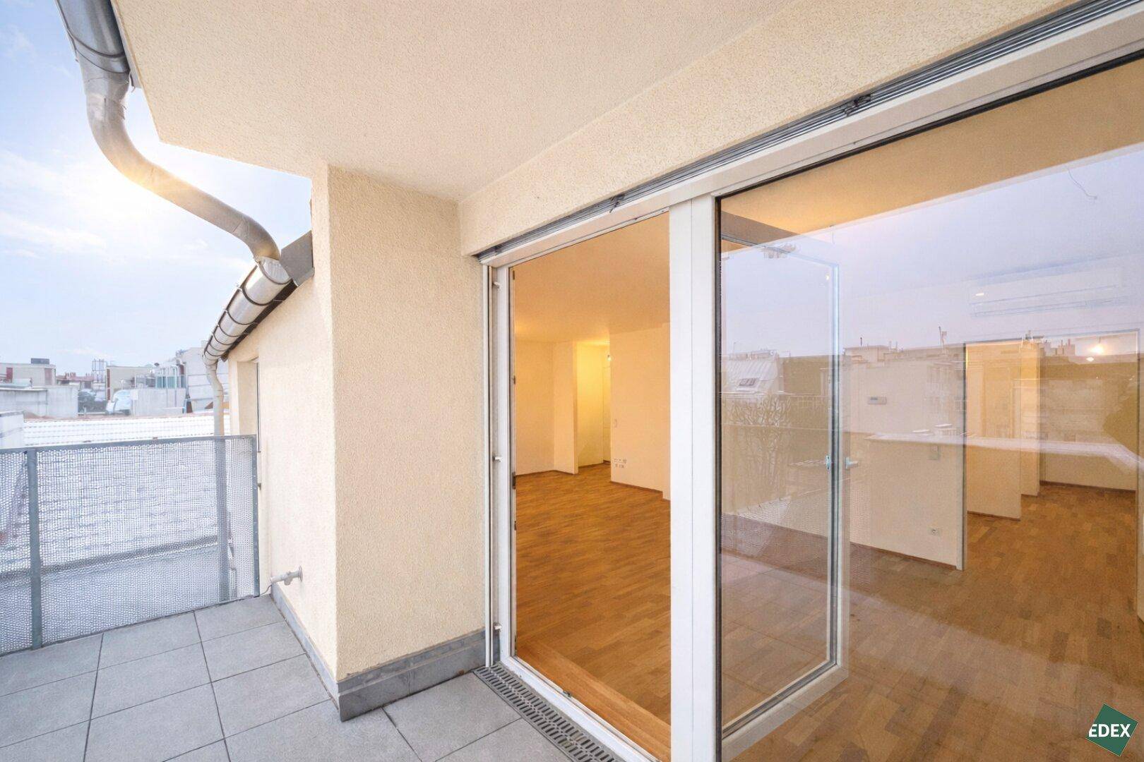 Balkon mit Zugang zu einem hellen Innenraum mit Holzfußboden und großen Glasschiebetüren.