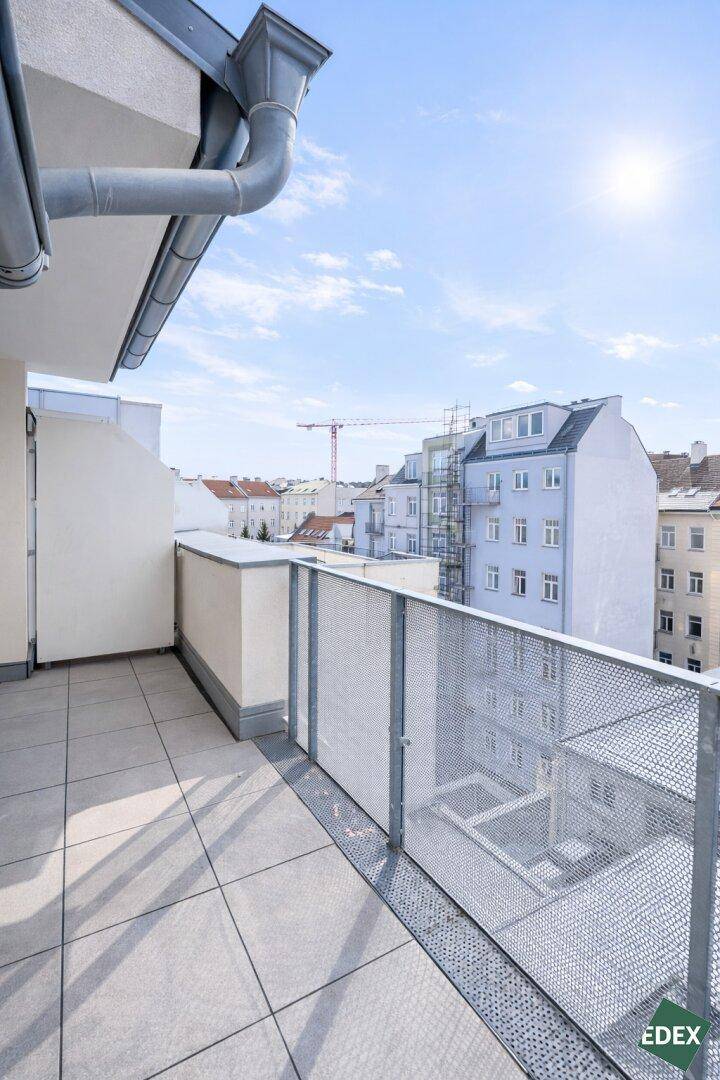 Sonniger Balkon mit Fliesenboden und Blick auf den Innenhof sowie die umliegenden Gebäude.