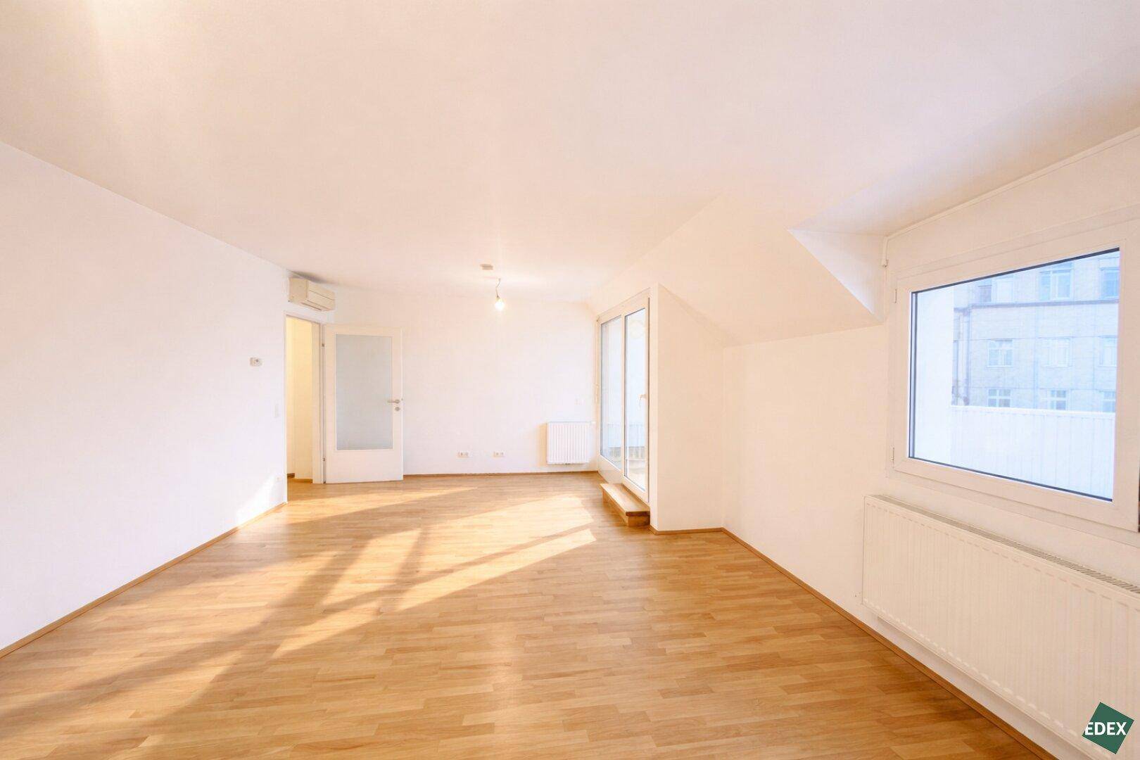 Lichtdurchflutetes Wohnzimmer mit Holzparkett, Heizkörpern und großzügigen Fenstern.