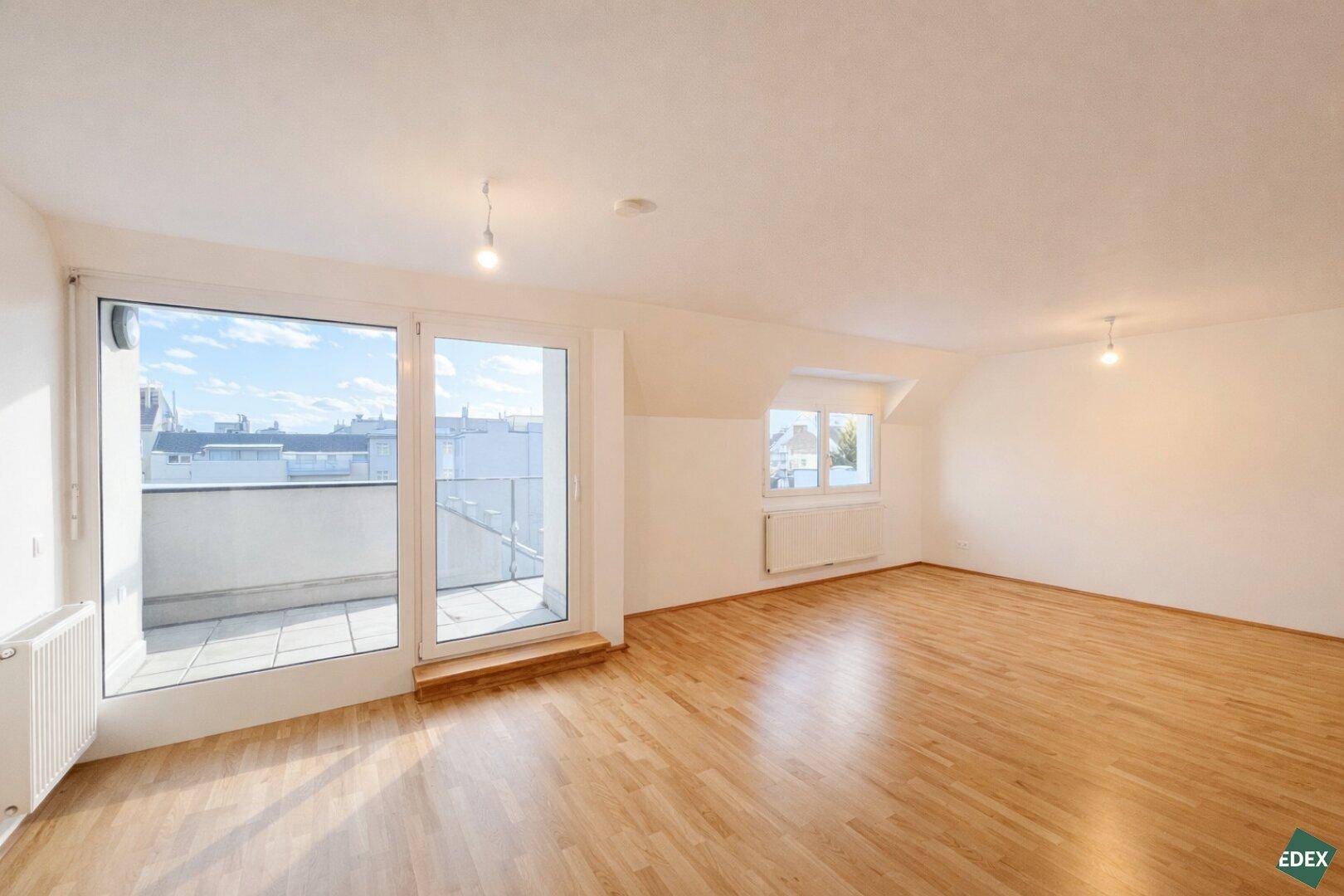 Helles Wohnzimmer mit Holzparkett, Dachschräge und Zugang zu einem Balkon.