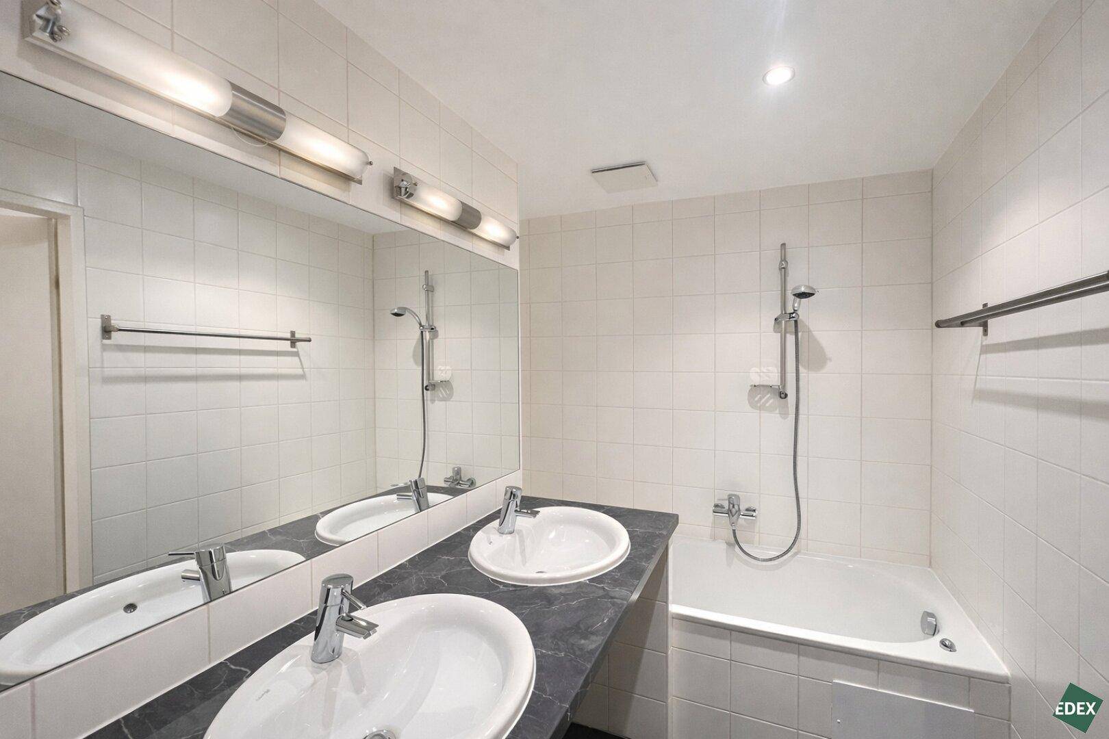 Helles Badezimmer mit Doppelwaschbecken, Badewanne und Duschfunktion, sowie großem Spiegel.