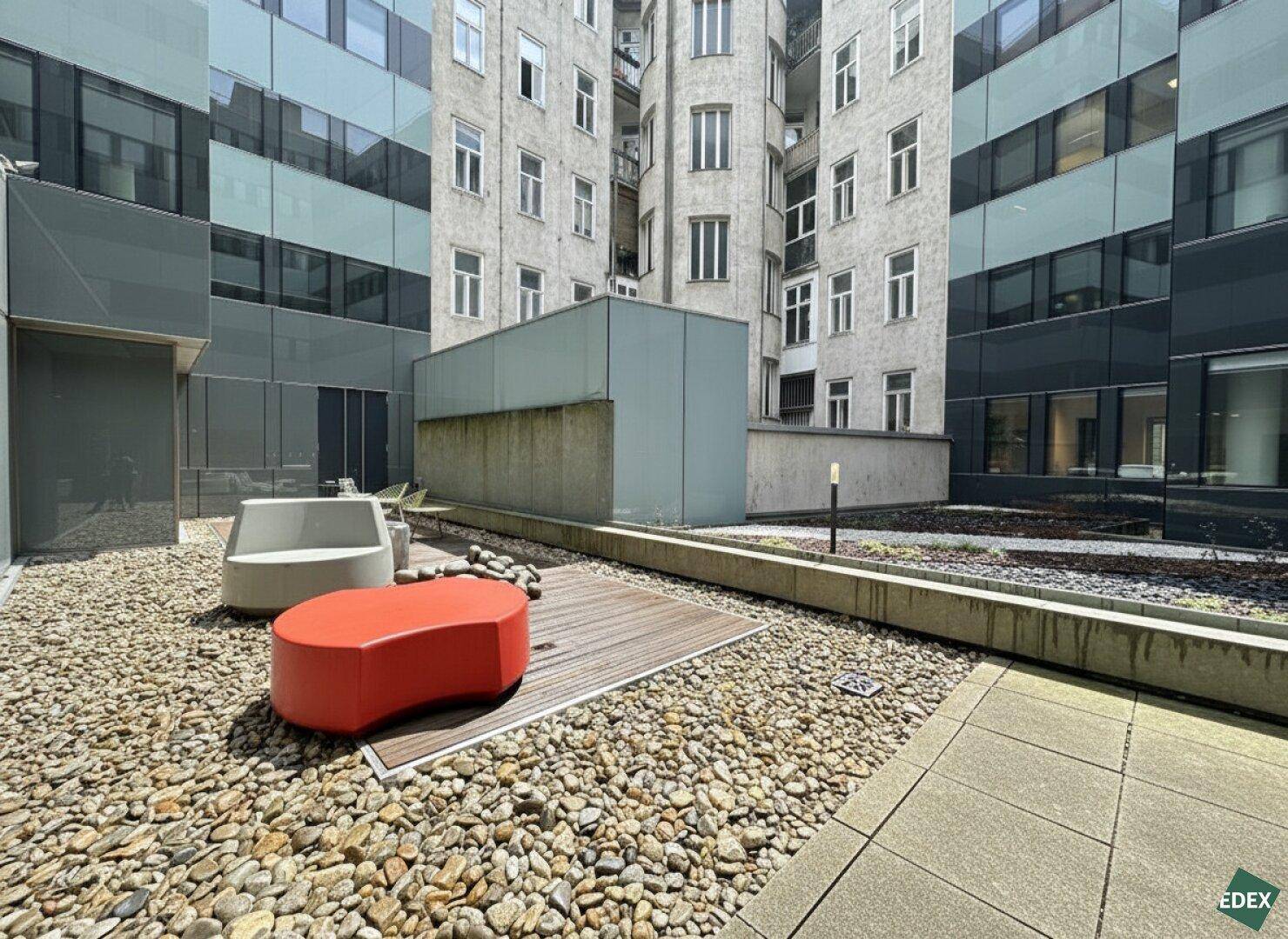 Attraktiver Innenhof mit modernen Sitzgelegenheiten, Kiesbeet und Holzdeck, umgeben von Gebäuden.