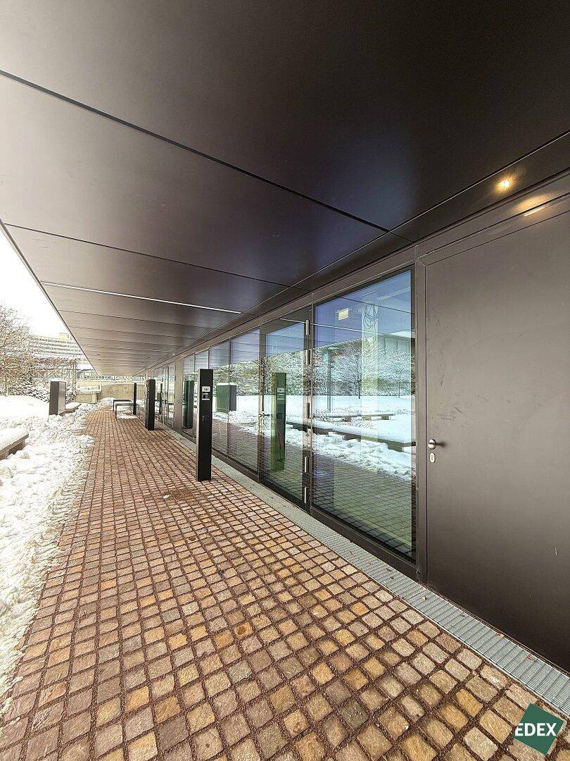 Moderne Gebäudefassade im Erdgeschoss mit großen Glasfronten und gepflastertem Gehweg im Schnee.