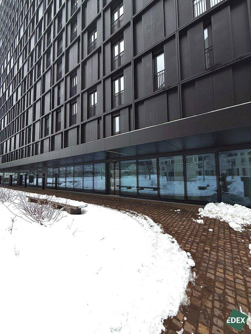 Moderne Gebäudefassade in dunklem Design mit vielen Fenstern und einem verschneiten Gehweg davor.