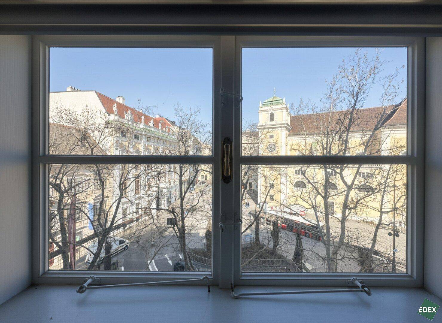 Blick aus einem Fenster auf eine belebte Stadtstraße mit historischen Gebäuden und Bäumen.