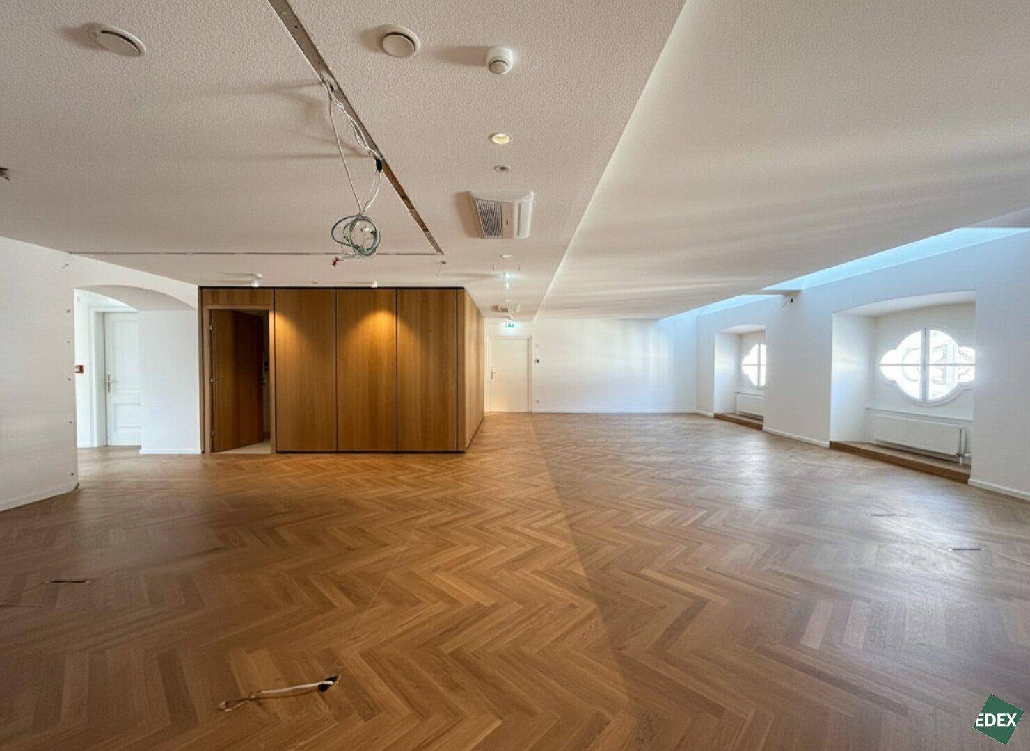 Großer, heller Büroraum mit Fischgrätparkett, weißen Wänden und einer eleganten Holzwandverkleidung.