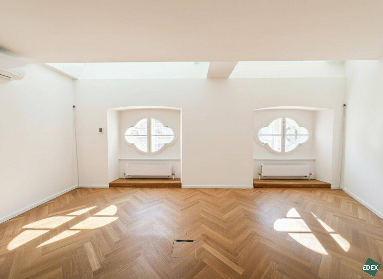 Detailansicht der dekorativen, ovalen Fenster in einem hellen Raum mit Fischgrätparkett und viel Sonnenlicht.