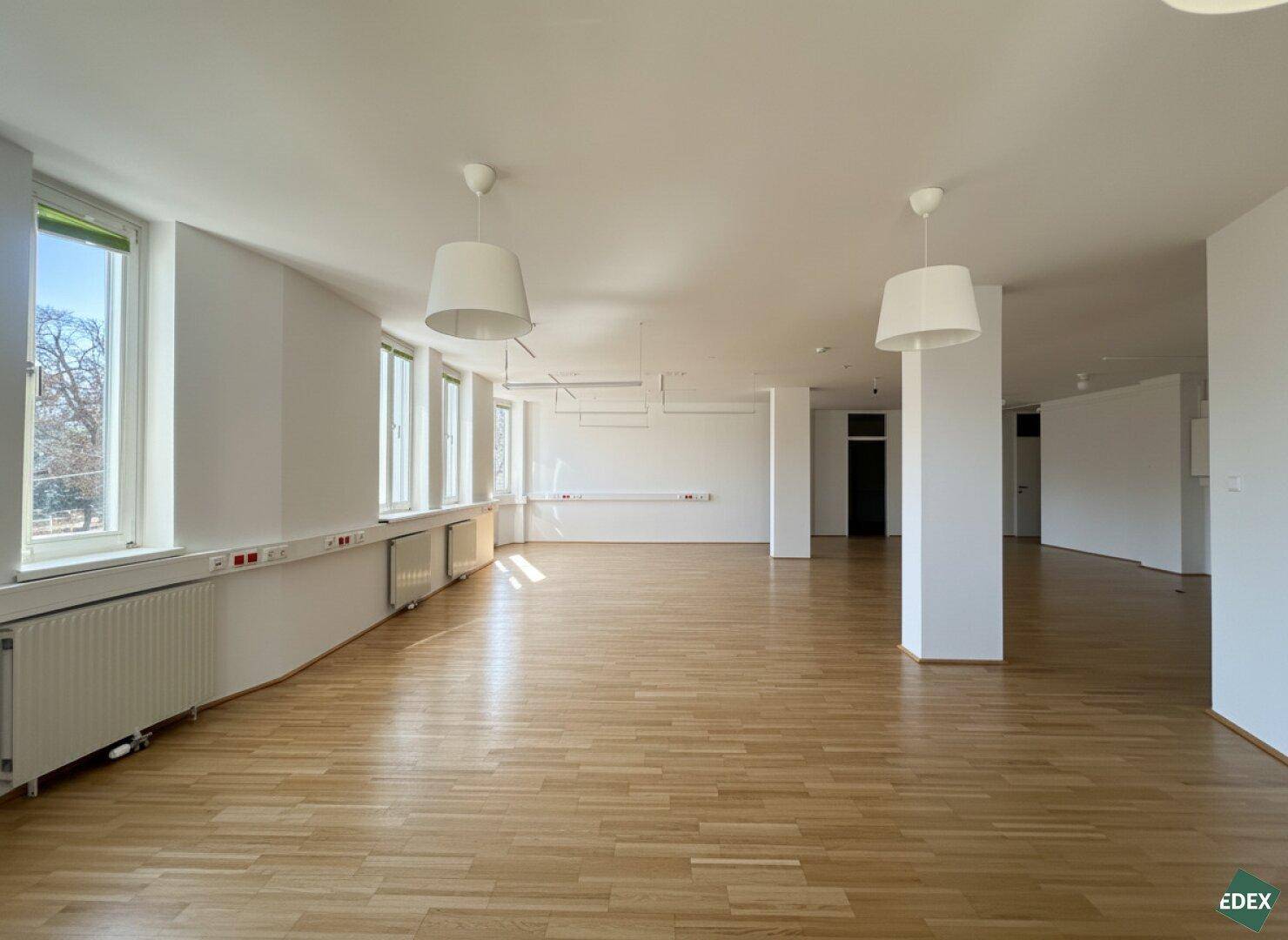 Heller Büroraum mit durchgehenden Fenstern, Parkettboden und modernen Deckenleuchten, bereit zur Nutzung.