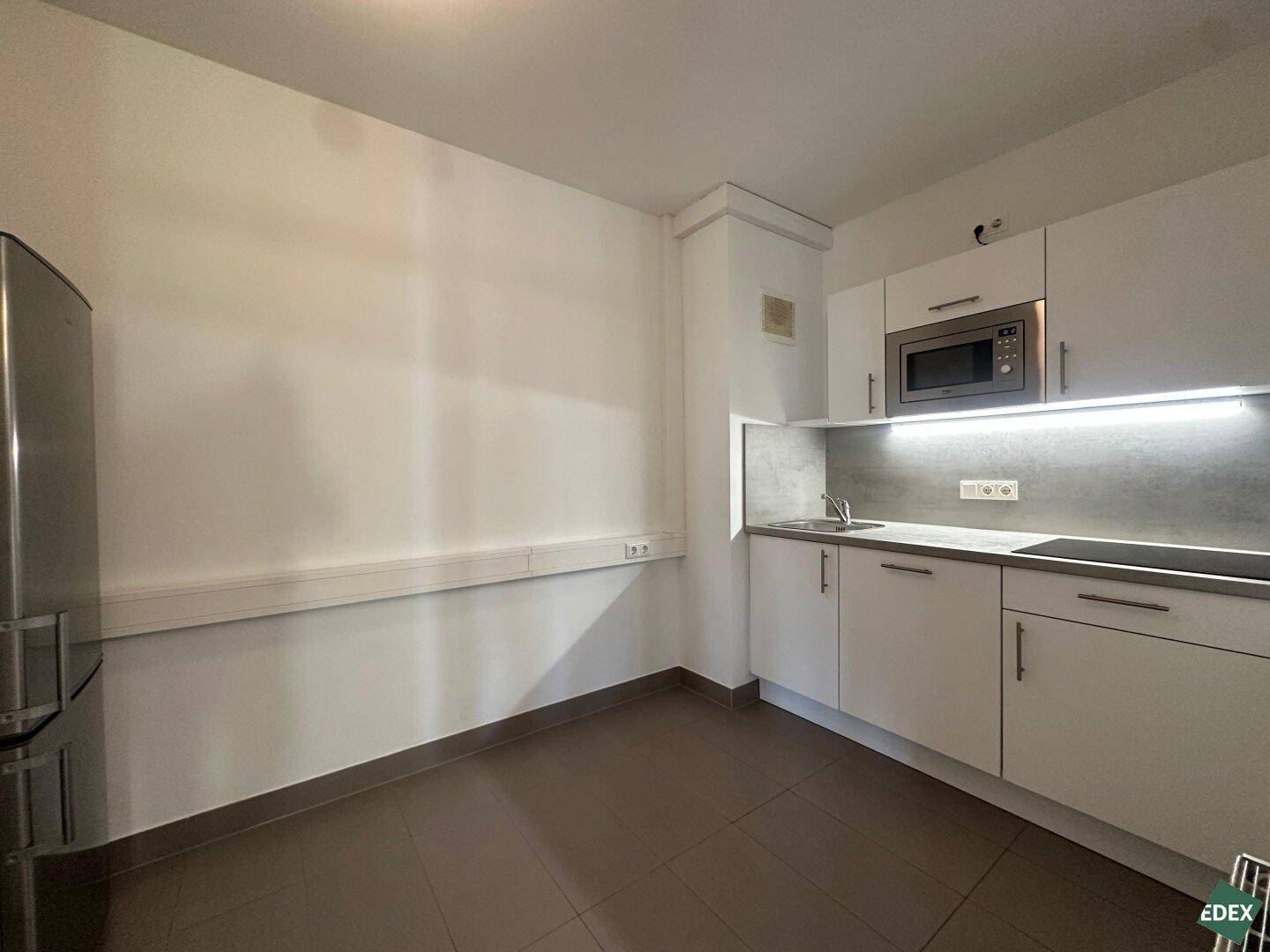 Moderne Teeküche mit weißen Schränken, Mikrowelle und Kühlschrank, ideal für Pausen.