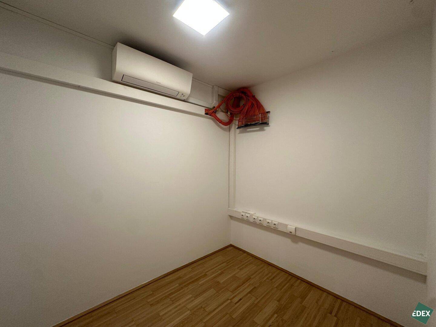 Kleiner Raum mit Klimaanlage und sichtbaren Kabelinstallationen, möglicherweise als Serverraum genutzt.