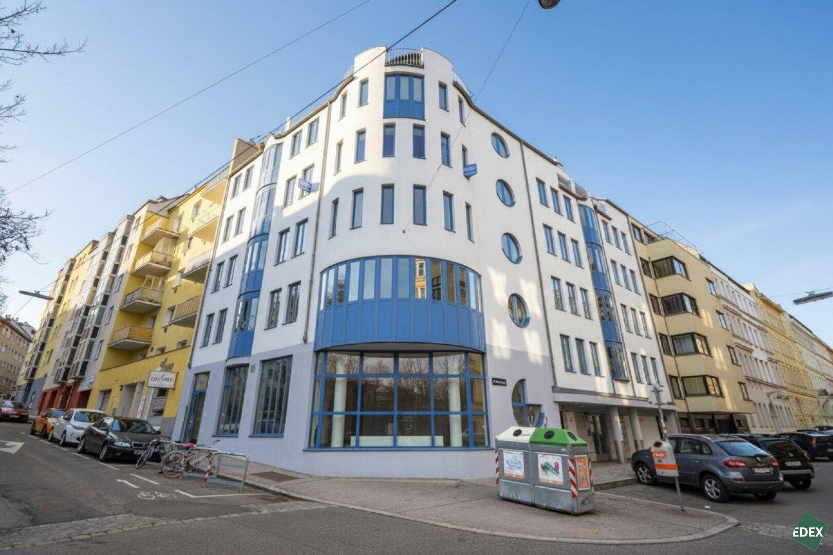 Modernes Eckgebäude mit blauen und weißen Fassadenelementen an einer städtischen Straße.