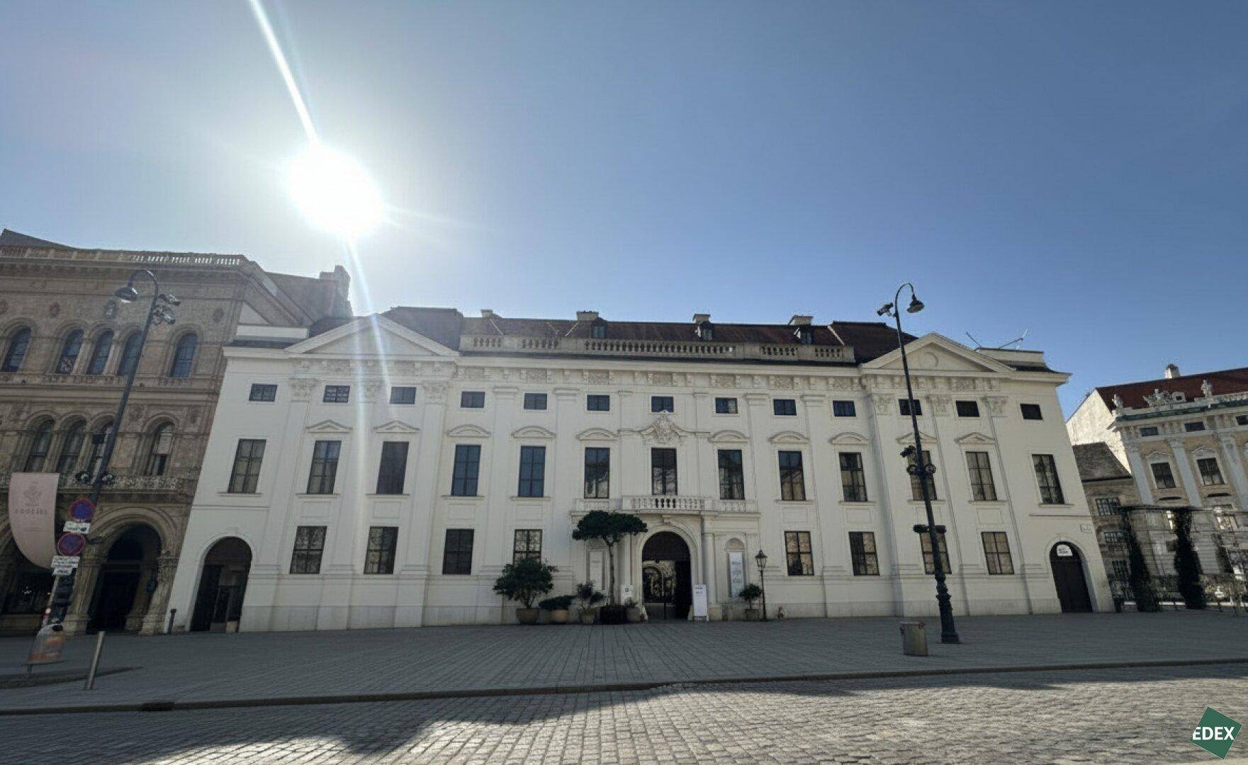 Prächtiges historisches Gebäude mit weißer Fassade und vielen Fenstern an einem sonnigen Tag.