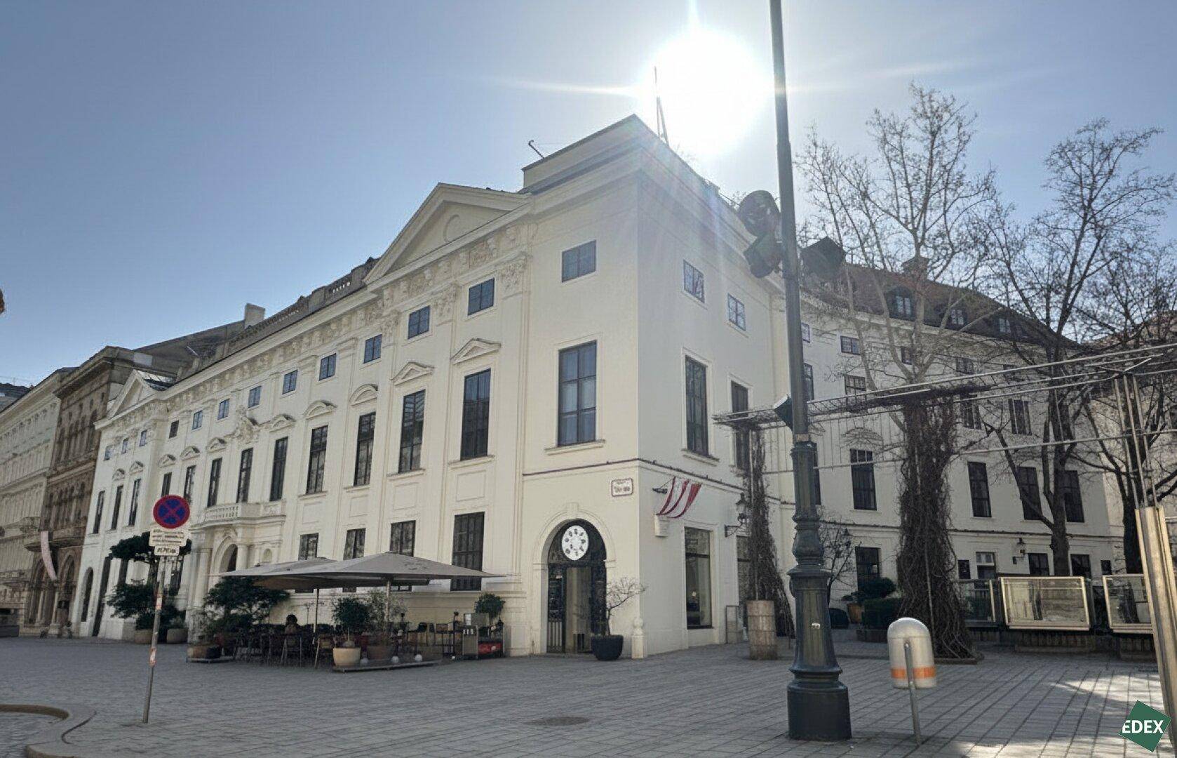 Historisches Gebäude mit weißer Fassade und einem charmanten Außenbereich mit Café an einer Straßenecke.