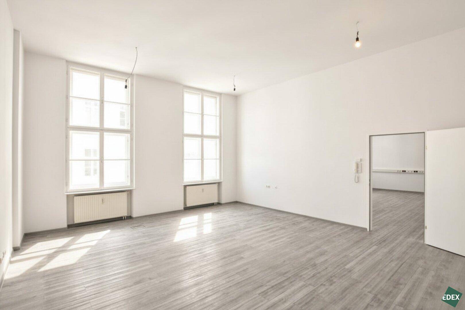 Großer, heller Büroraum mit zwei hohen Fenstern, die den Raum mit natürlichem Licht durchfluten.