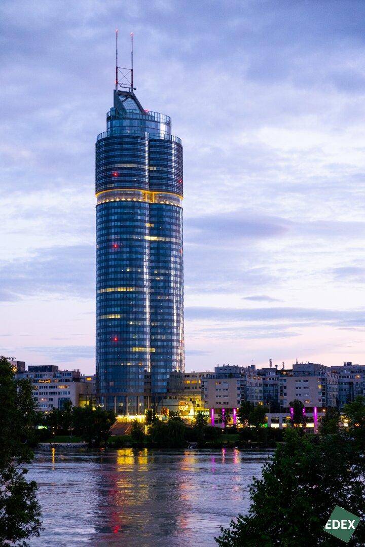 Beeindruckendes modernes Hochhaus bei Sonnenuntergang, beleuchtet und am Ufer eines Gewässers gelegen.