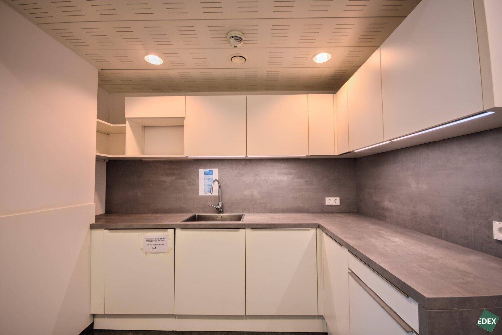 Moderne Teeküche mit weißen Schränken, Spüle und Arbeitsplatte, ideal für Mitarbeiter.