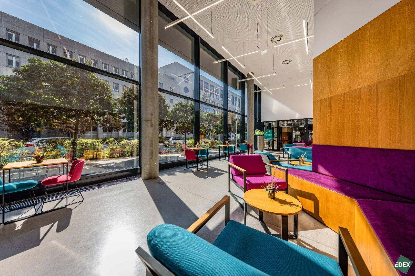Farbenfroher Loungebereich mit großen Fenstern und modernen Möbeln, ideal für entspannte Treffen.