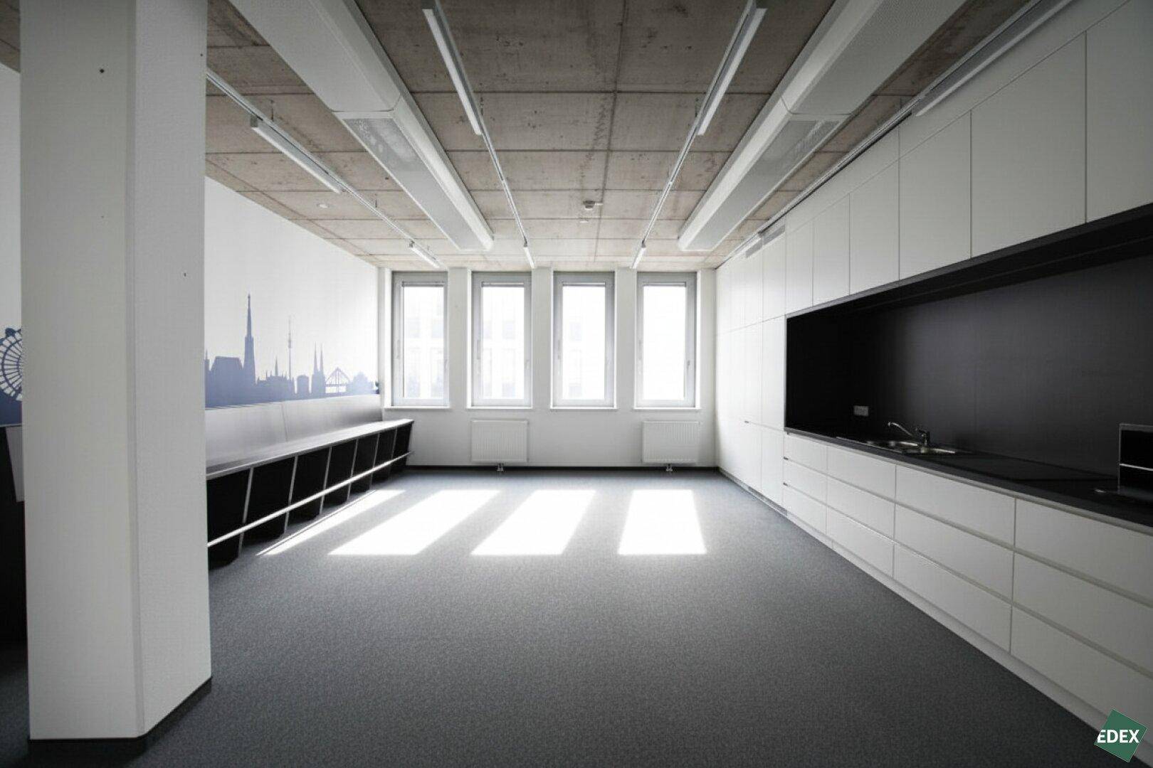 Moderne Büroküche mit weißen Schränken, dunkler Arbeitsplatte und Blick auf die Stadt.