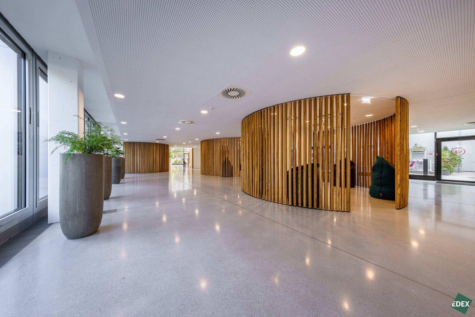Elegante Lobby mit Holzlamellenwänden, glänzendem Boden und großen Pflanzenkübeln.