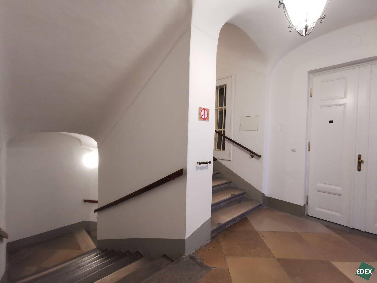 Historisches Treppenhaus mit Holzgeländer und Fliesenboden, das den Charme des Altbaus widerspiegelt.