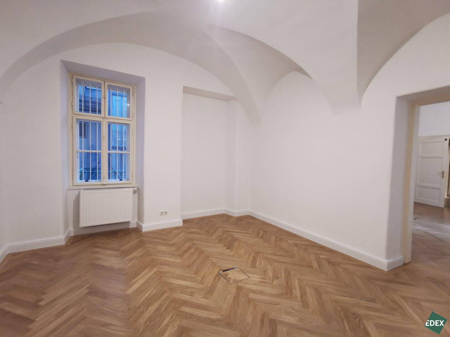 Raum mit historischem Charme, Fischgrätparkett, einem Fenster und einem beeindruckenden Gewölbedecke.