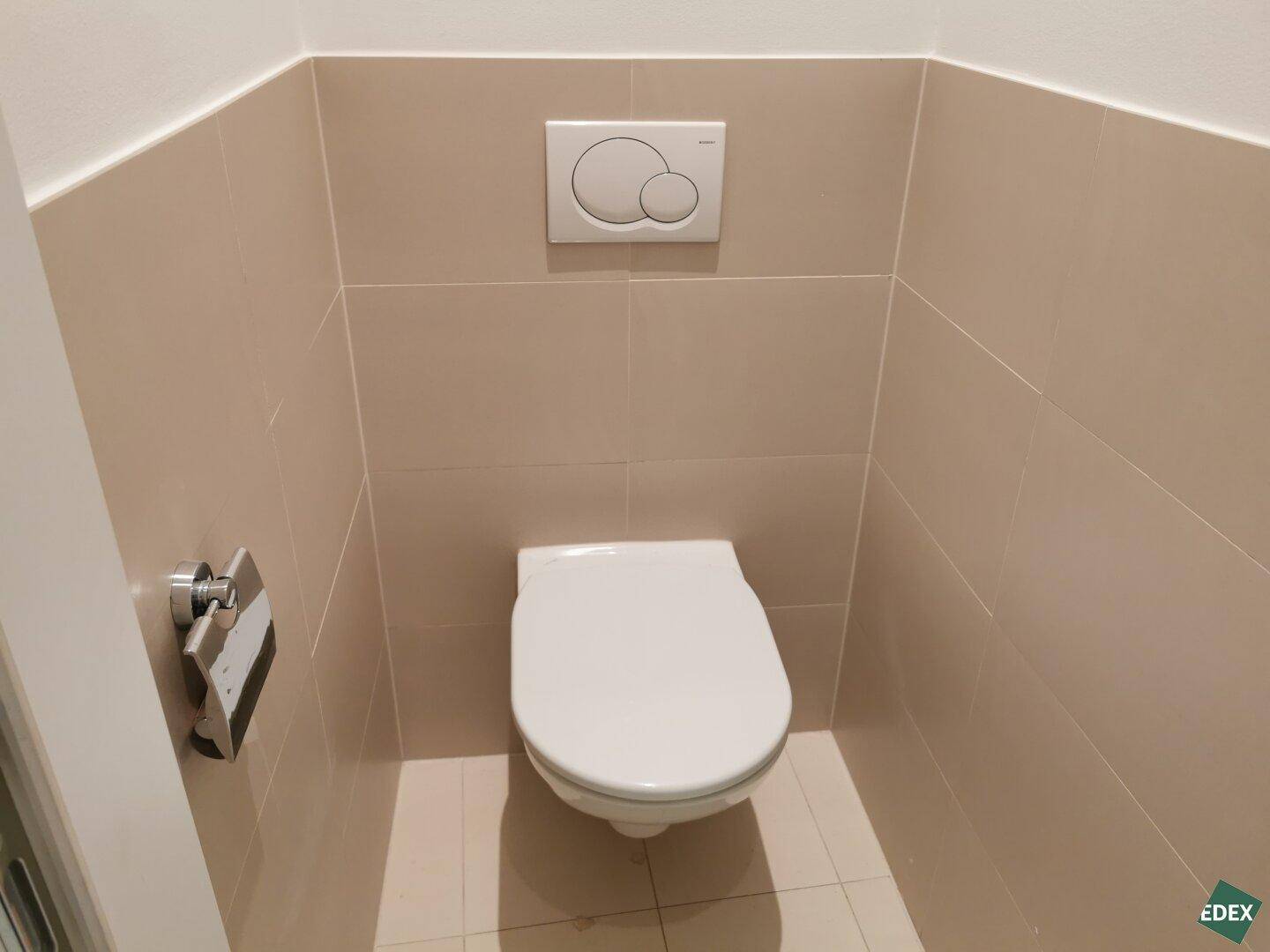 Saubere Toilette mit wandhängendem WC und beigefarbenen Fliesen an den Wänden, in gutem Zustand.