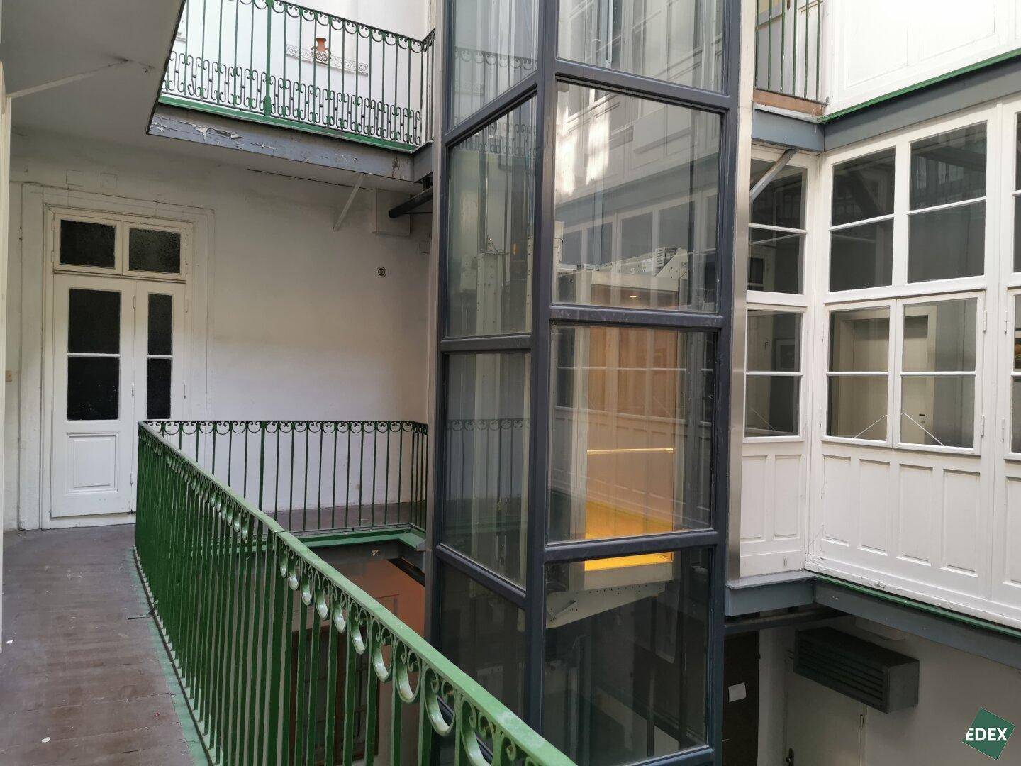Glasaufzug in einem Innenhof, der die verschiedenen Etagen des Gebäudes miteinander verbindet.