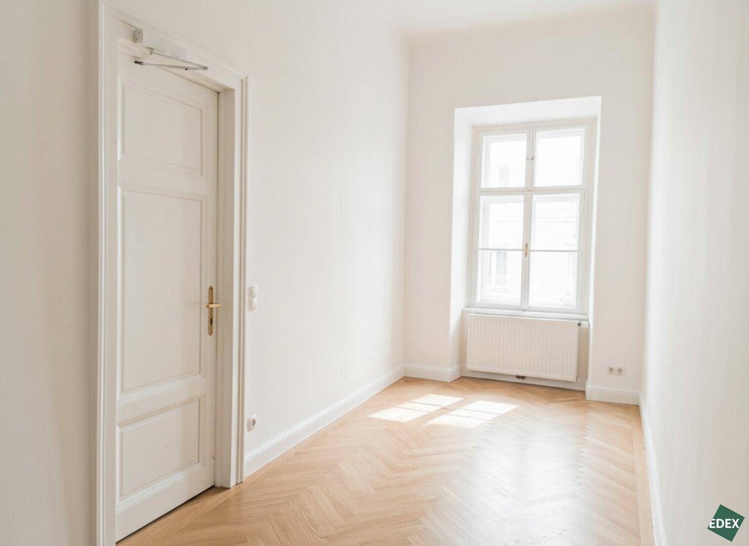 Schmaler Raum mit Fischgrätparkett, einem Fenster und einer weißen Tür, ideal als Flur oder kleines Büro.