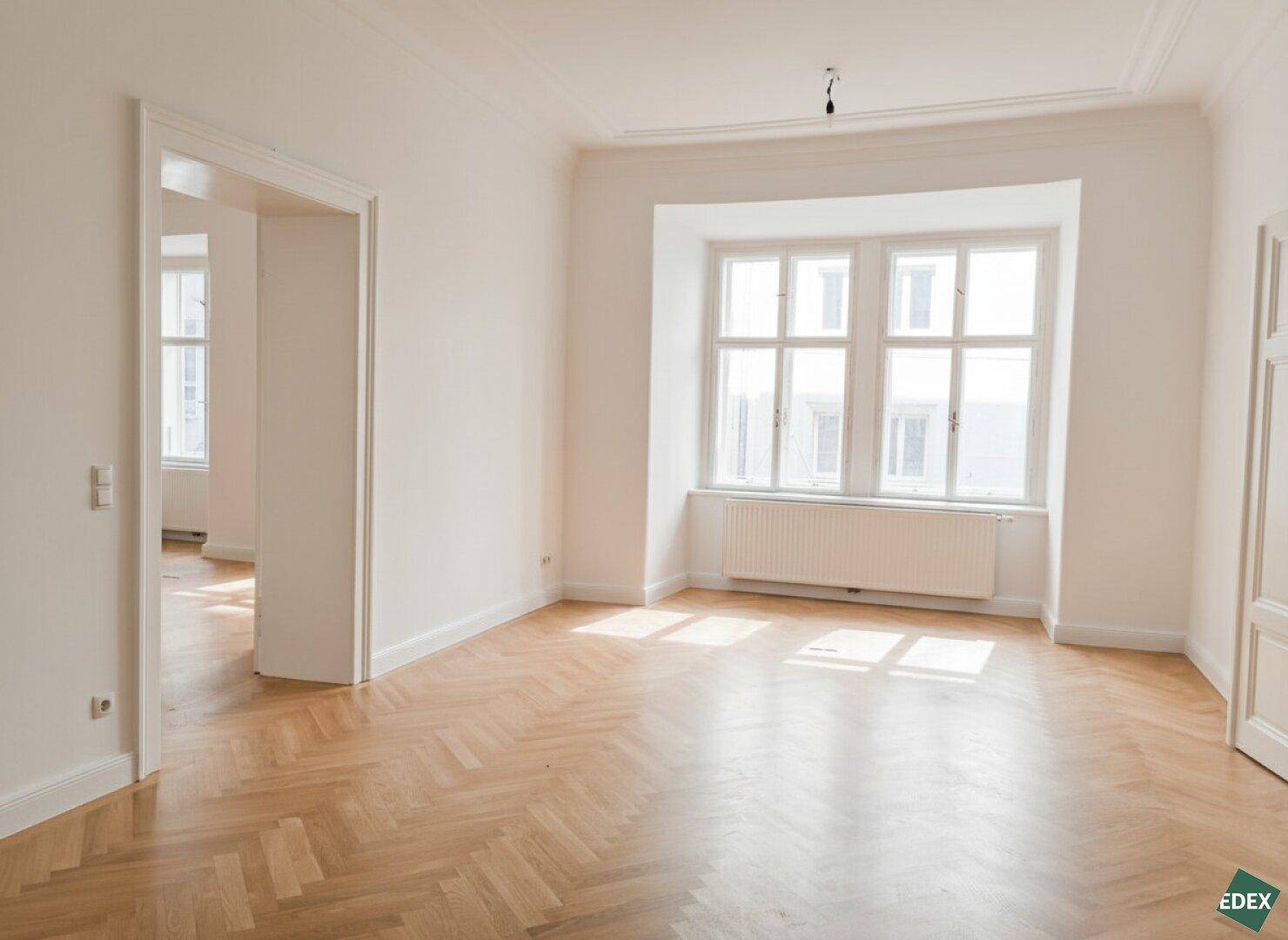 Großer, heller Raum mit Fischgrätparkett und einem breiten Fenster, das den Raum mit Sonnenlicht füllt.