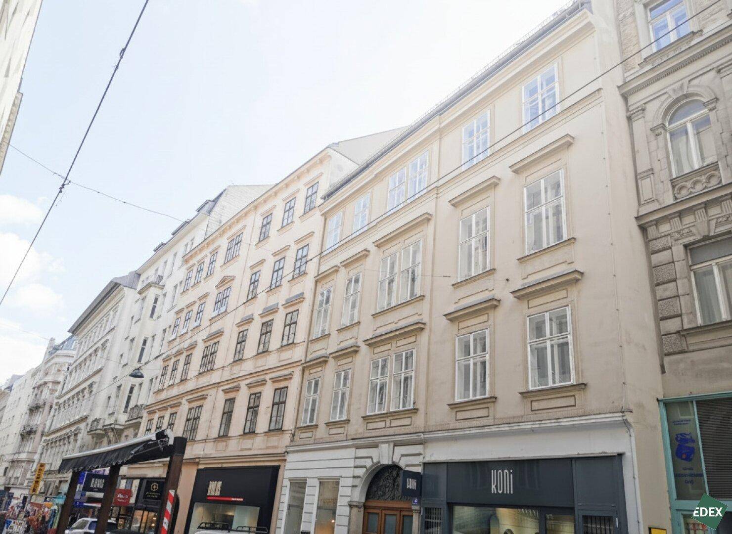 Klassische Altbaufassade an einer belebten Straße mit vielen Fenstern und Geschäften im Erdgeschoss.